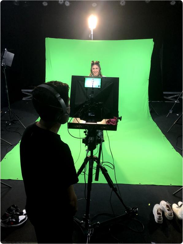 Atriz sendo filmada com um pano de fundo e uma pessoa analisando as imagens