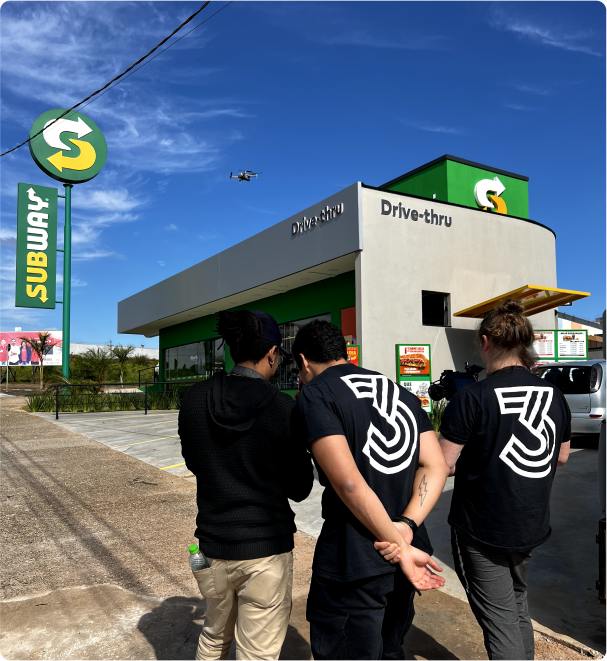 Três homens da empresa '3 Creative Content' verificando uma foto na câmera próximo a um restaurante do subway